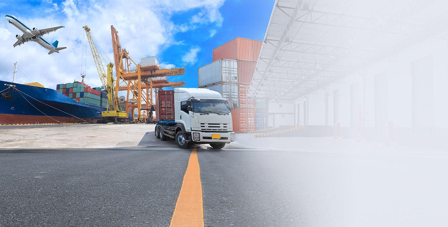 Truck parked on a dock next to cargo containers and a cargo ship with an airplane flying above